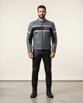 A man modeling a gray leather motorcycle jacket with black and white stripe details, paired with black leather pants and boots, standing against a plain beige studio background.