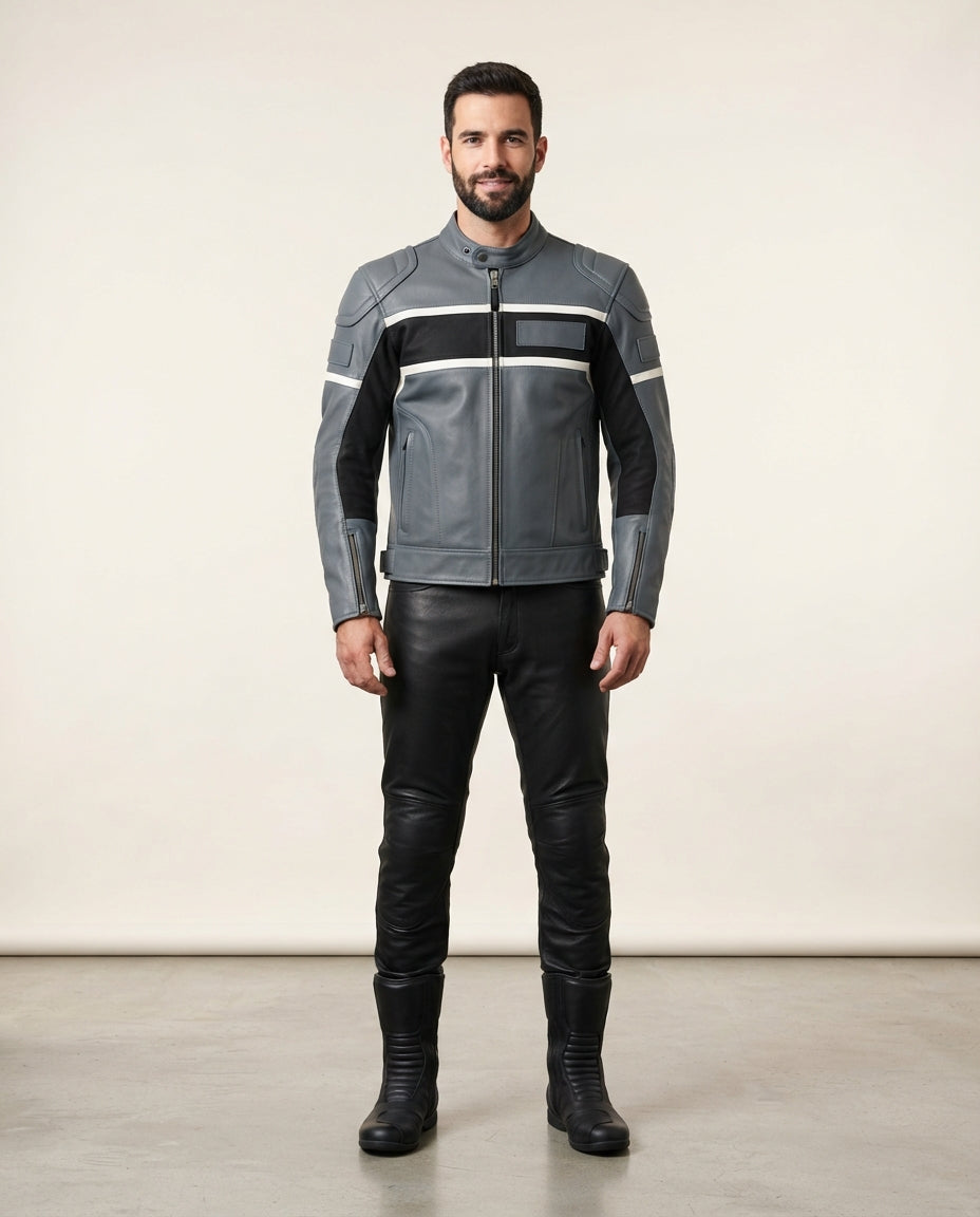 A man modeling a gray leather motorcycle jacket with black and white stripe details, paired with black leather pants and boots, standing against a plain beige studio background.