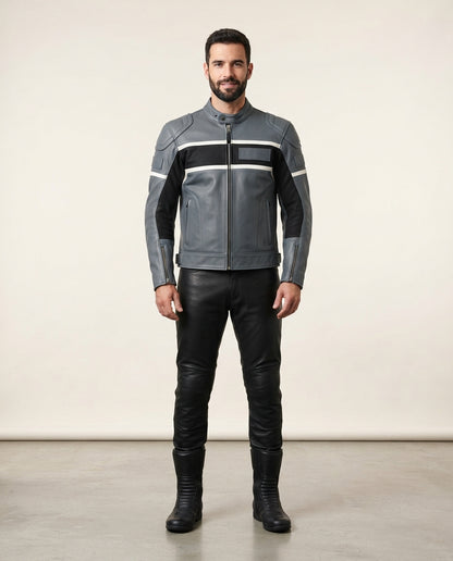 A man modeling a gray leather motorcycle jacket with black and white stripe details, paired with black leather pants and boots, standing against a plain beige studio background.